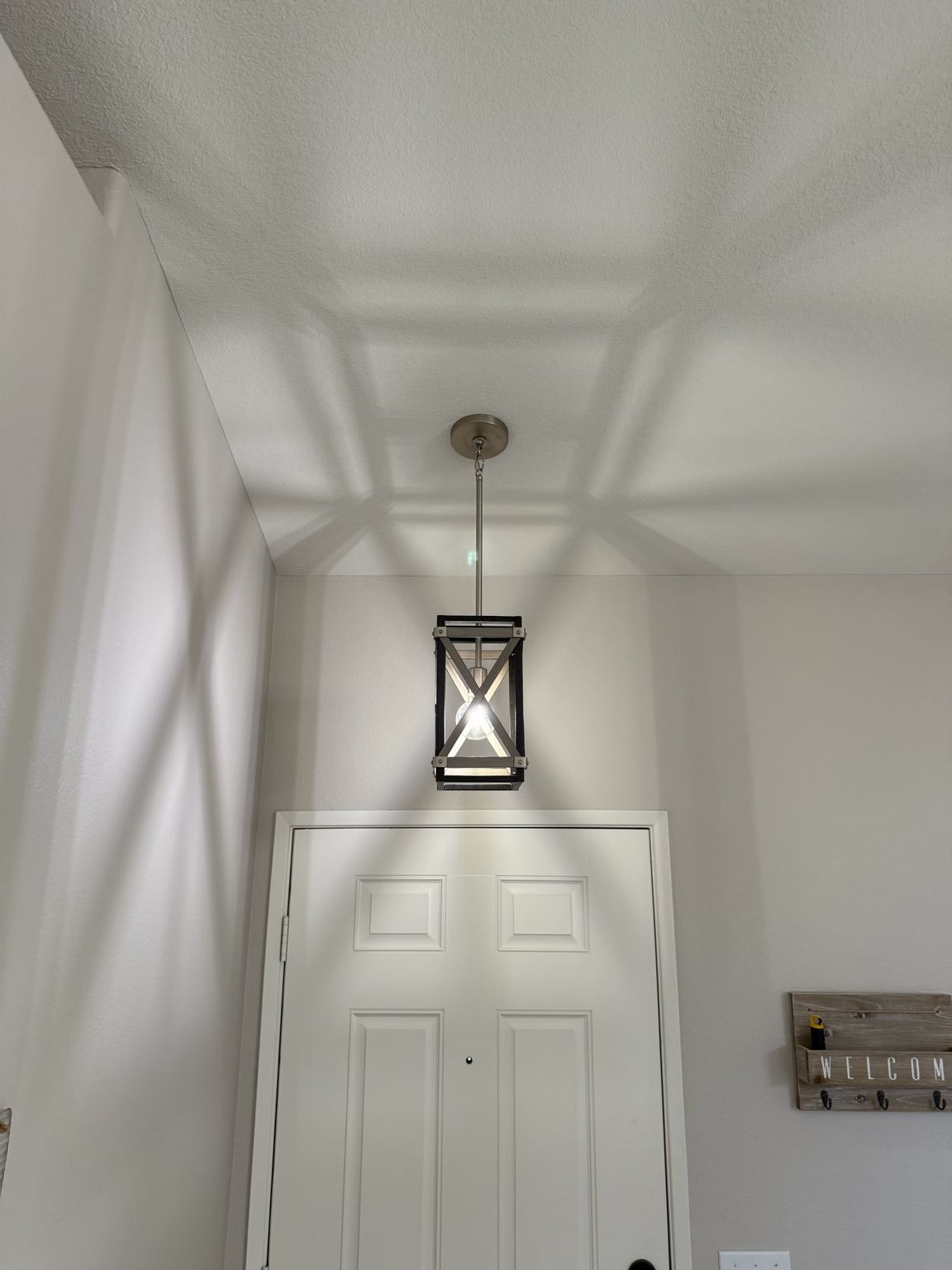 A rectangular, lantern-style pendant light hangs above a white door, casting distinct geometric shadows on the ceiling.