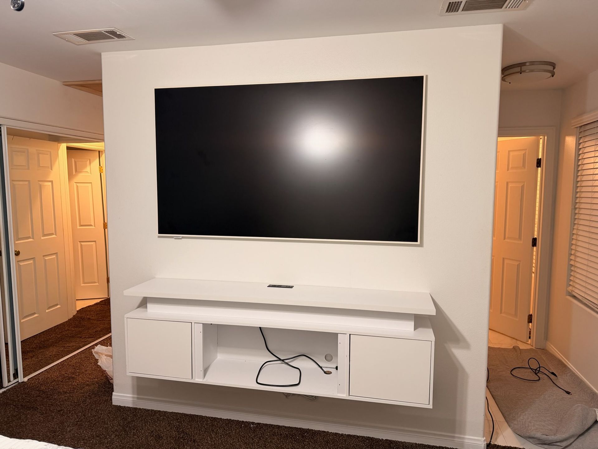 A wall-mounted television hangs above a minimalist white floating entertainment console in a room with doorways.