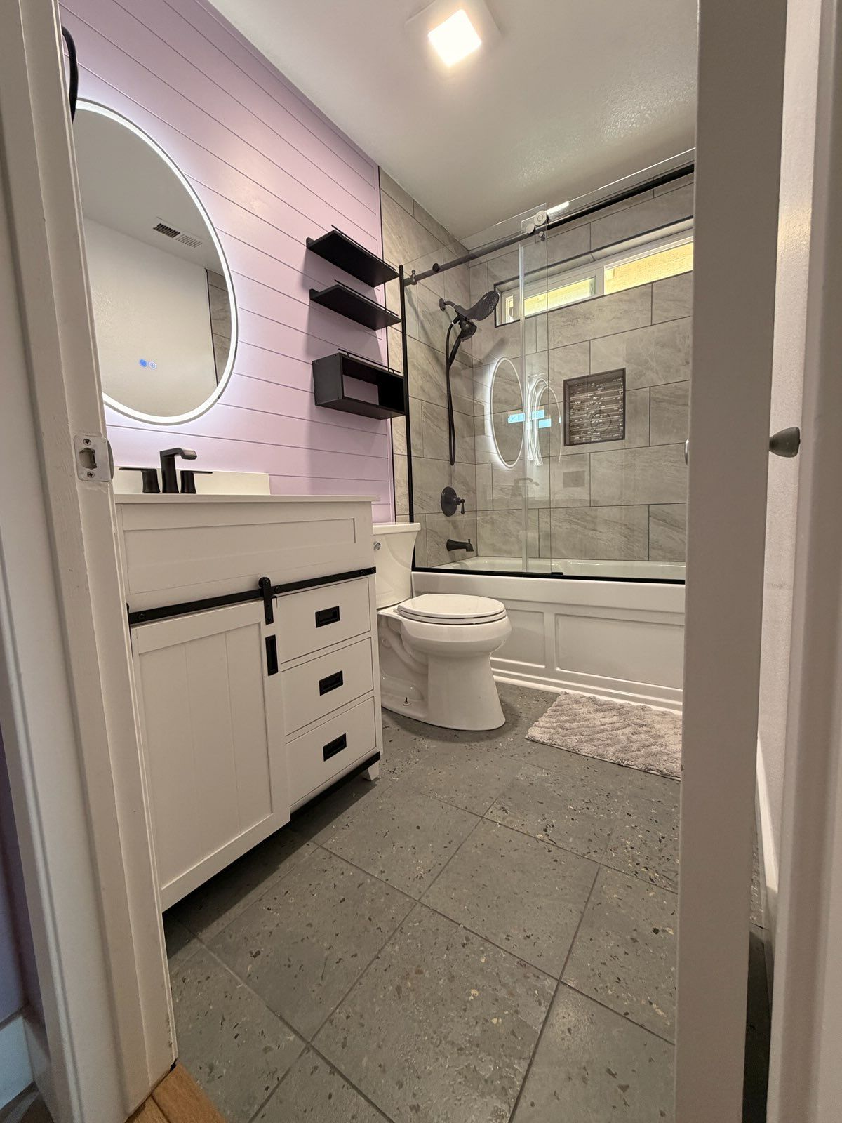 A modern bathroom featuring a white vanity with black hardware, a light purple shiplap wall, and a gray tiled floor.