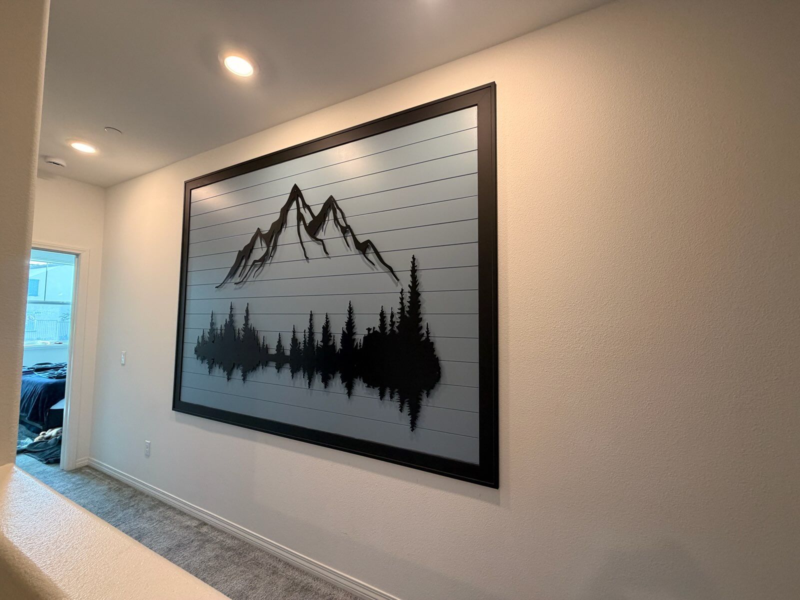 Large framed wall art featuring a black silhouette of mountains and pine trees reflected over water on a grey background.