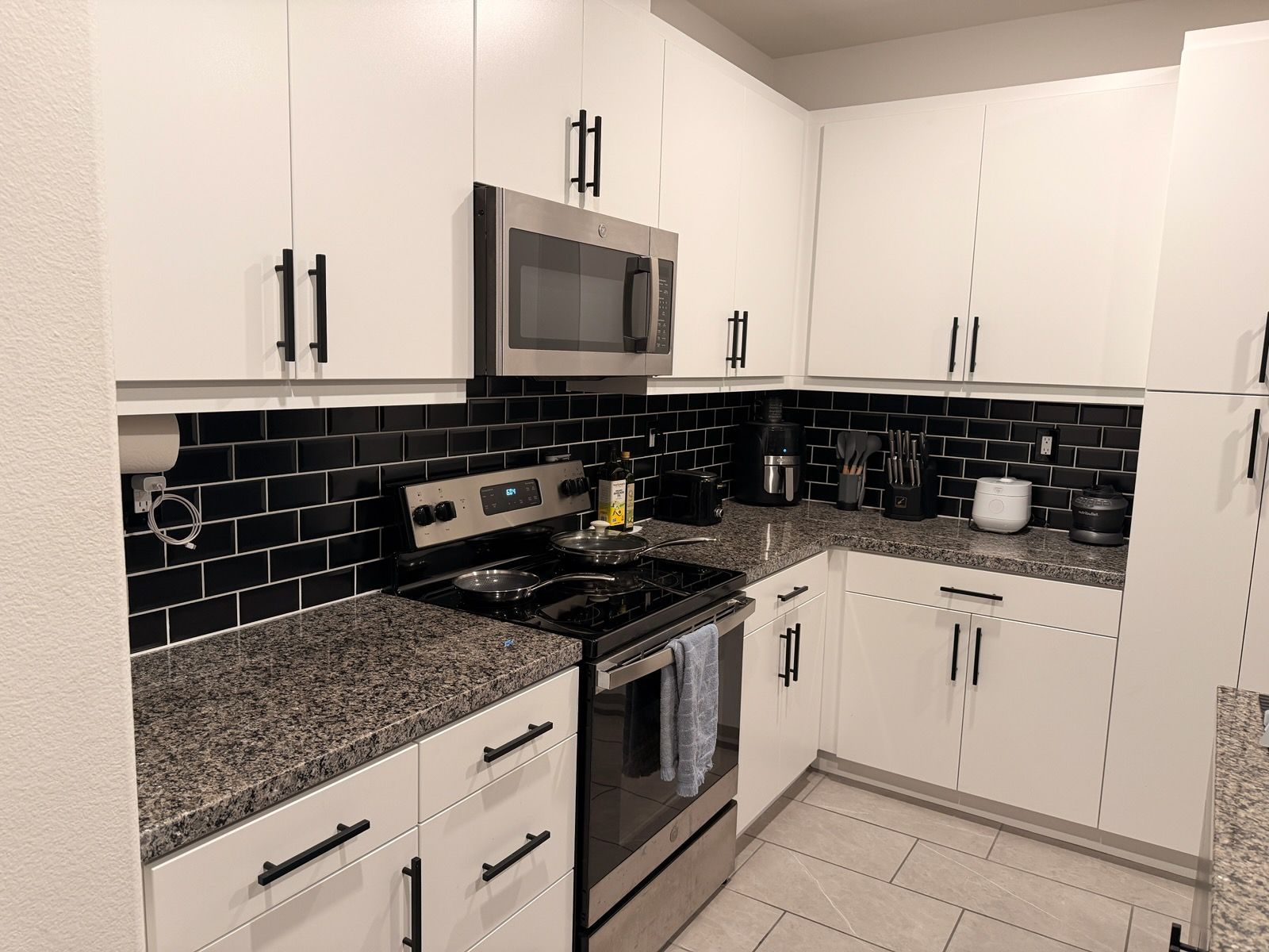 A kitchen with white cabinets, dark subway tile backsplash, granite countertops, and stainless steel appliances.