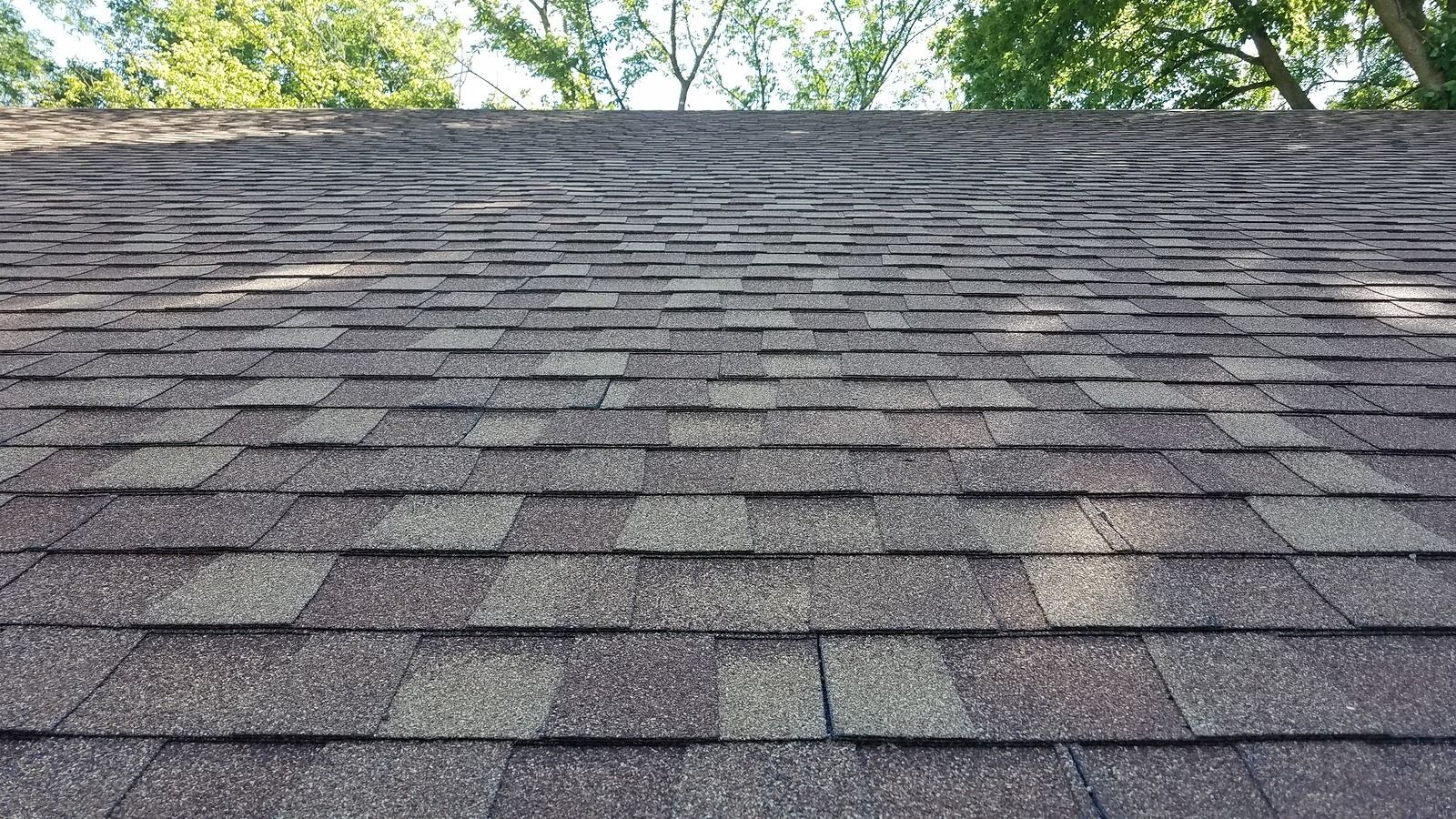 Brown asphalt shingle roof with varying shades, trees in the background.