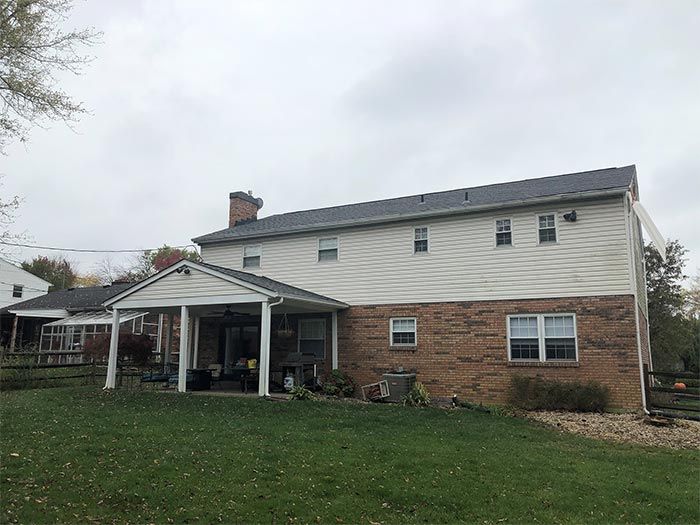 Back of a two-story house with a covered patio, brick and siding, on a cloudy day.