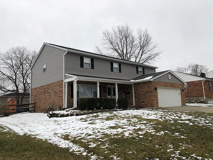Two-story house with gray siding upper level and brick lower level, snow on the ground.