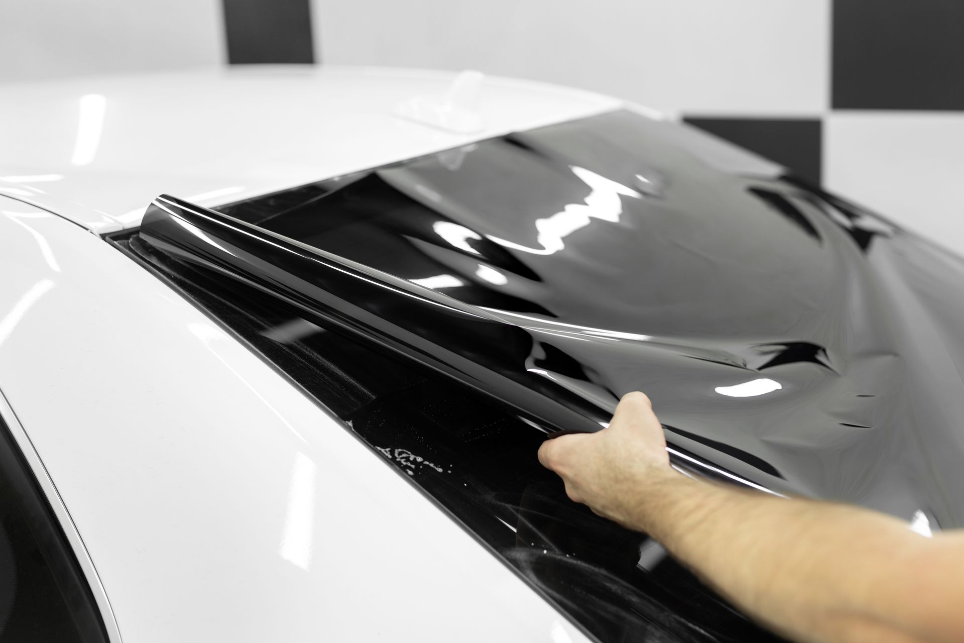 Hand applying black film to a white car windshield in a garage