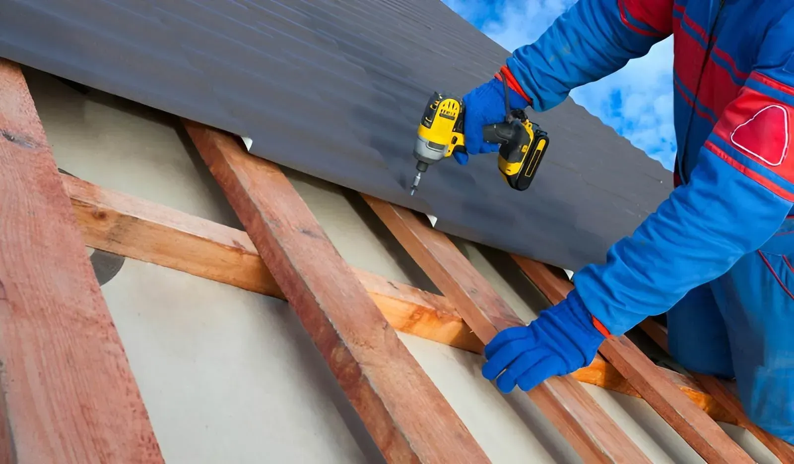 A Person Uses a Yellow Power Drill to Secure a Dark Roof Panel — Dunnrite Plumbing Services in Airlie Beach, QLD