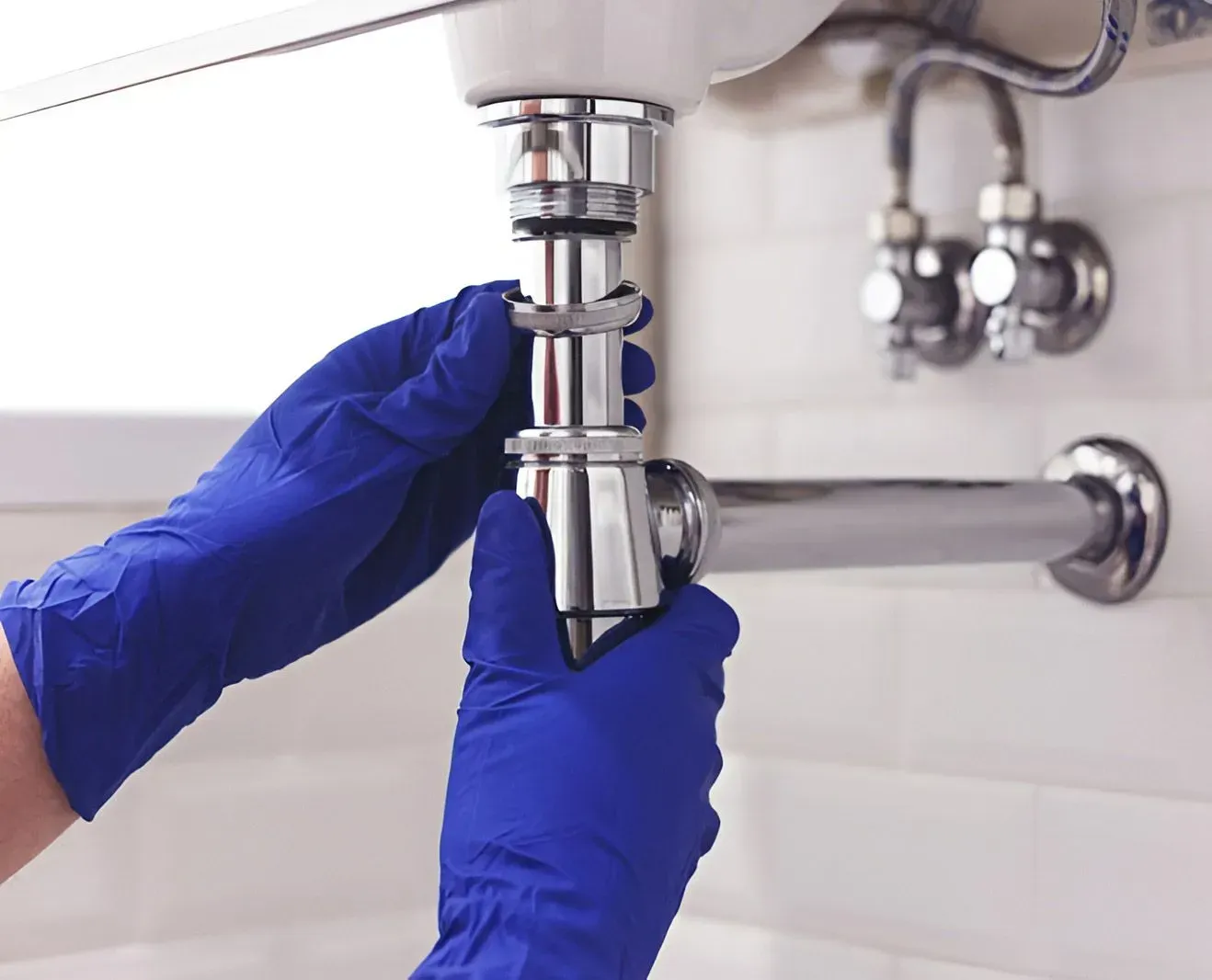A Person Wearing Blue Gloves Fixing the Chrome P-trap — Dunnrite Plumbing Services in Cannonvale, QLD