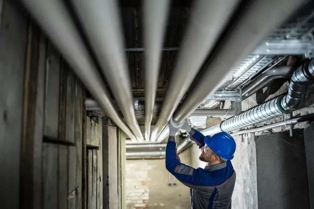 A Technician Inspects Overhead Industrial Pipes in a Utility Basement — Dunnrite Plumbing Services in Airlie Beach, QLD