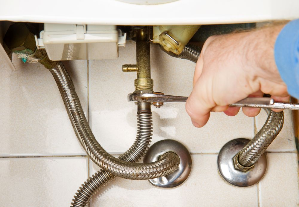 A Person Uses a Wrench to Tighten a Metal Nut on a Plumbing Fixture — Dunnrite Plumbing Services in Cannonvale, QLD