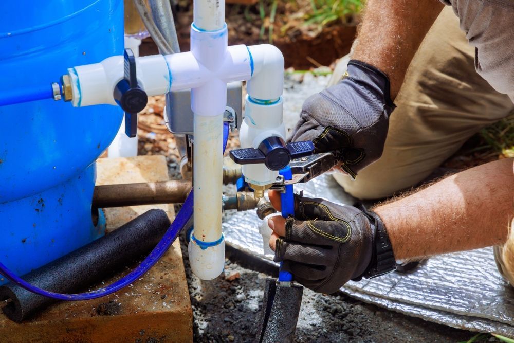 A Person in Work Gloves Uses Pliers to Adjust a Blue Plastic Pipe — Dunnrite Plumbing Services in Cannonvale, QLD