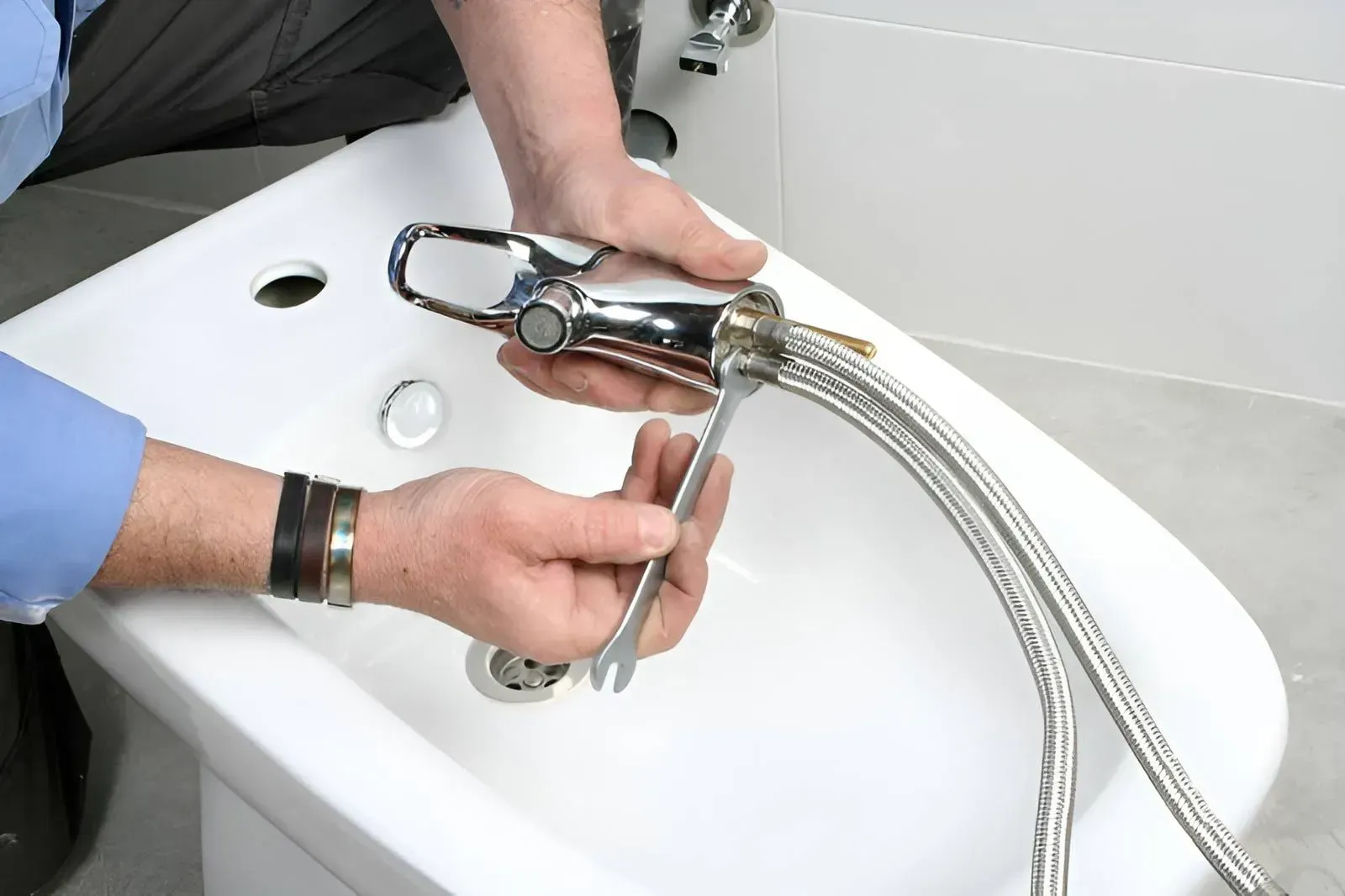 A Person Uses a Small Wrench to Tighten a Metal Supply Hose — Dunnrite Plumbing Services in Proserpine, QLD