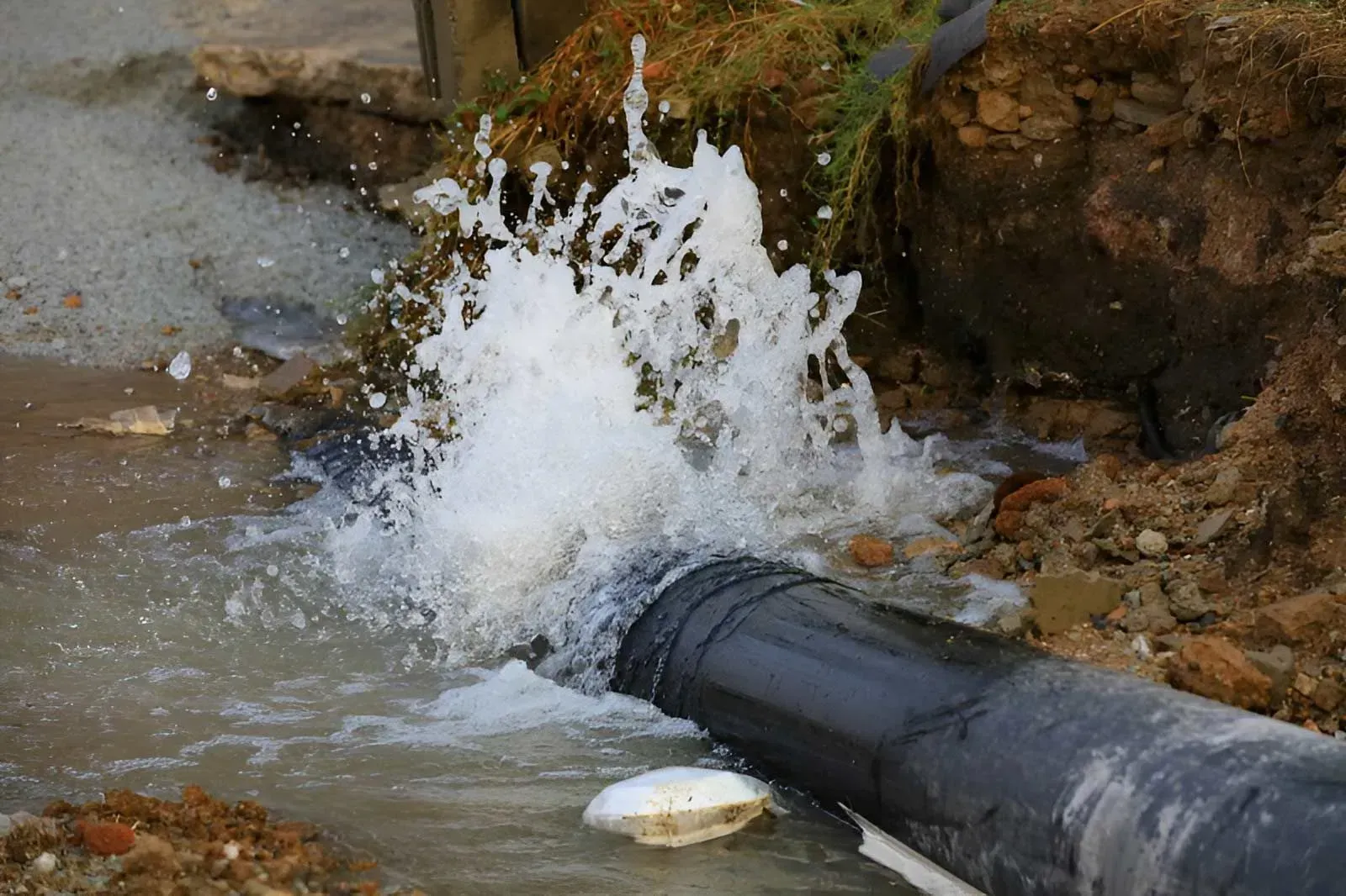 A Thick, Dark Pipe Lies on the Ground as Water Sprays Forcefully — Dunnrite Plumbing Services in Airlie Beach, QLD