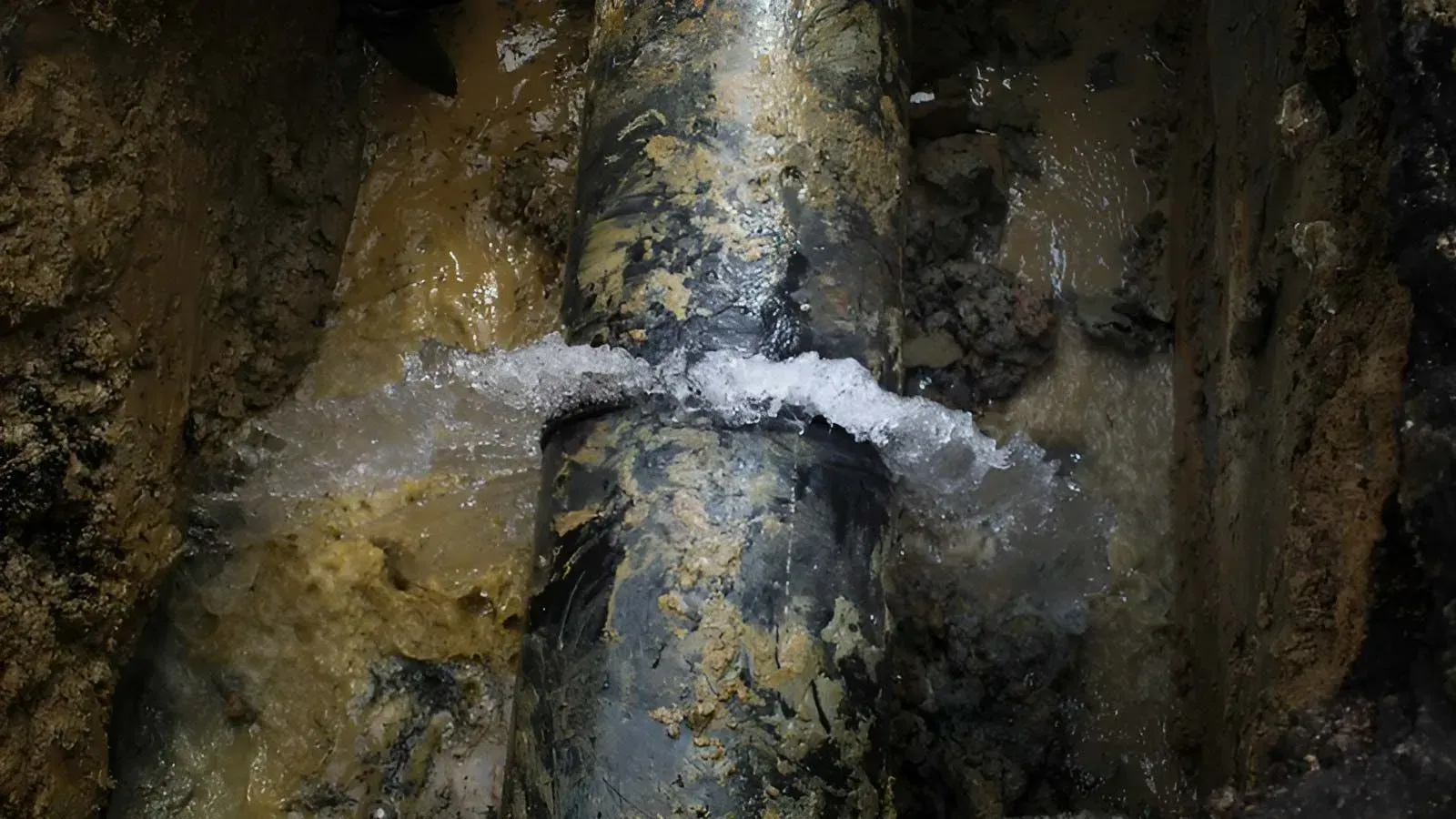 Water Spraying From a Pressurized Pipe Leak in a Narrow Dirt Trench — Dunnrite Plumbing Services in Cannonvale, QLD