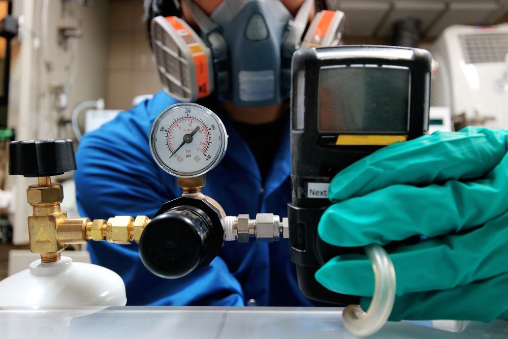 A Person in a Respirator and Blue Coveralls Holds a Gas Monitor — Dunnrite Plumbing Services in Airlie Beach, QLD