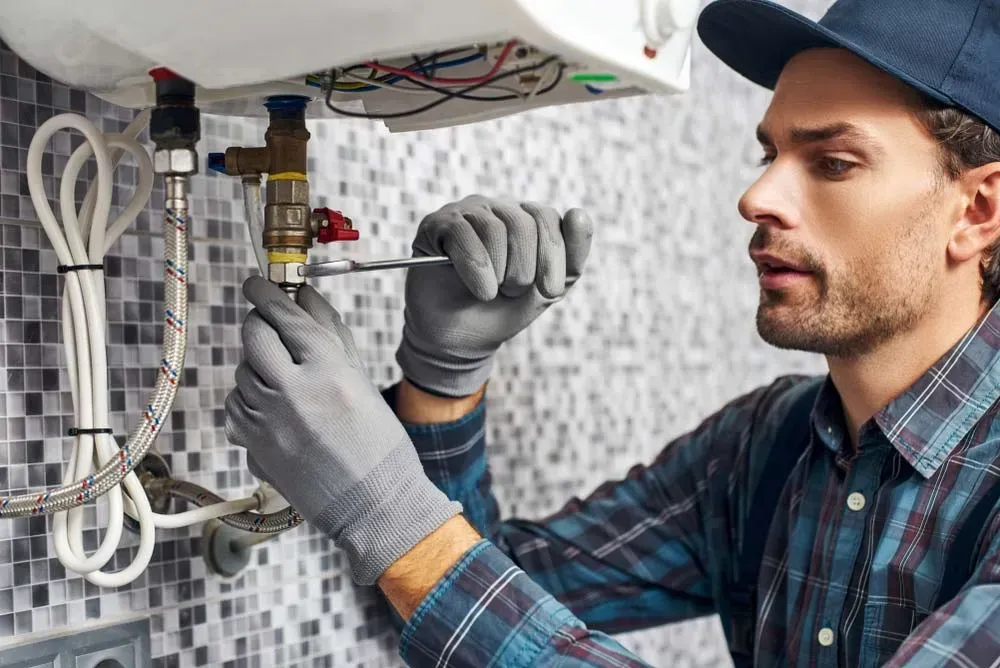 A Person in A Plaid Shirt and Cap Uses a Wrench to Repair Plumbing — Dunnrite Plumbing Services in Airlie Beach, QLD