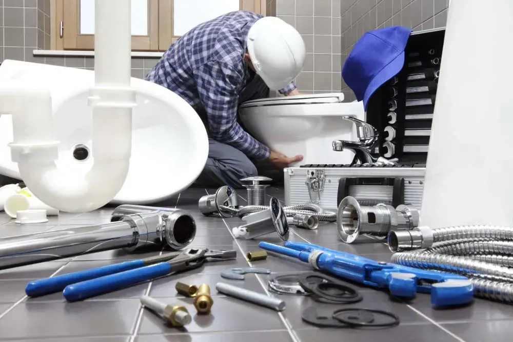 A Plumber in a Hard Hat Kneeling on a Tiled Floor to Install a Toilet — Dunnrite Plumbing Services in Cannonvale, QLD