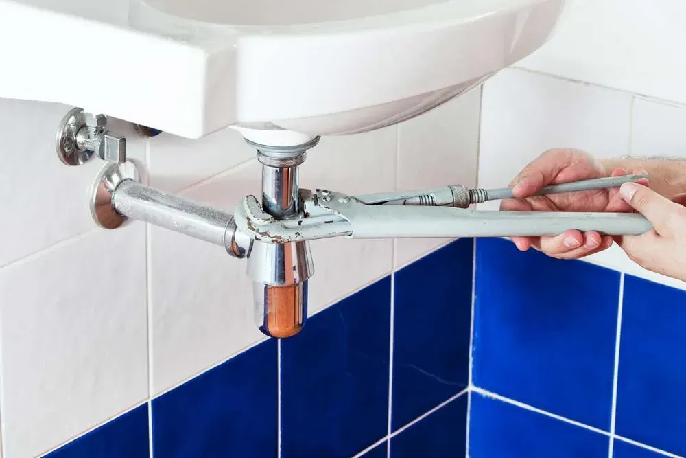 Hands Using a Wrench to Repair a Chrome Sink Drain Pipe — Dunnrite Plumbing Services in Cannonvale, QLD