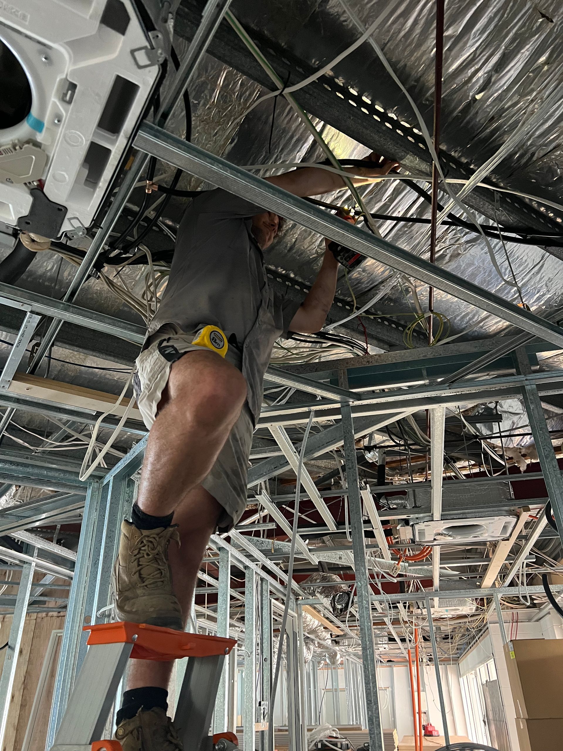 A Worker on a Step Ladder Installs Piping and Components — Dunnrite Plumbing Services in Cannonvale, QLD
