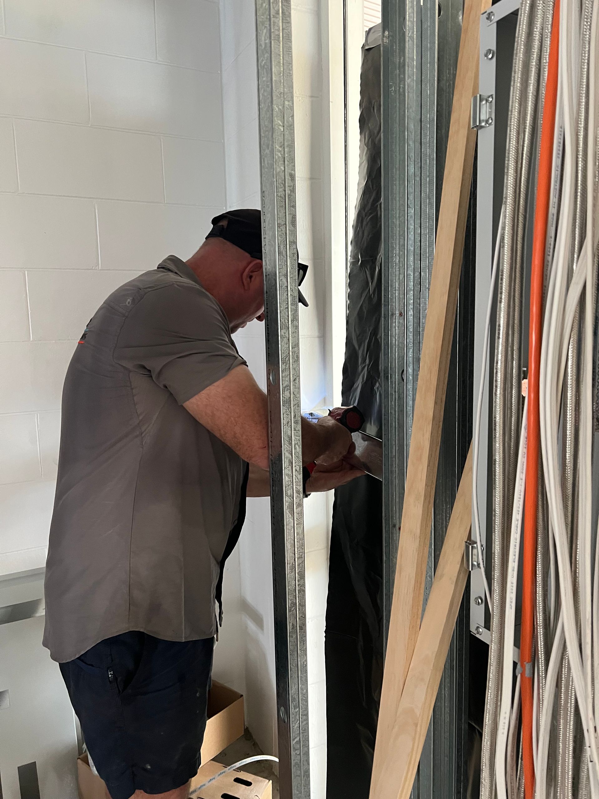 A Person Wearing a Grey Shirt and Cap Works on Wiring — Dunnrite Plumbing Services in Cannonvale, QLD