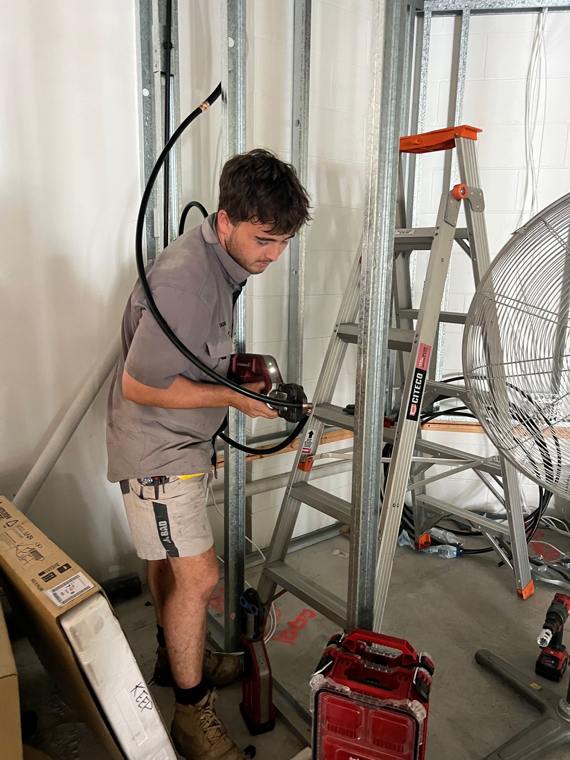 A Person in a Gray Shirt and Shorts Uses a Powered Tool — Dunnrite Plumbing Services in Airlie Beach, QLD