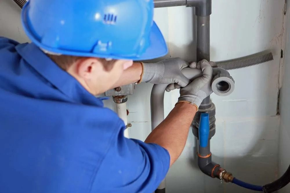 A Worker in a Blue Uniform and Hard Hat Repairing Plumbing Pipes — Dunnrite Plumbing Services in Cannonvale, QLD