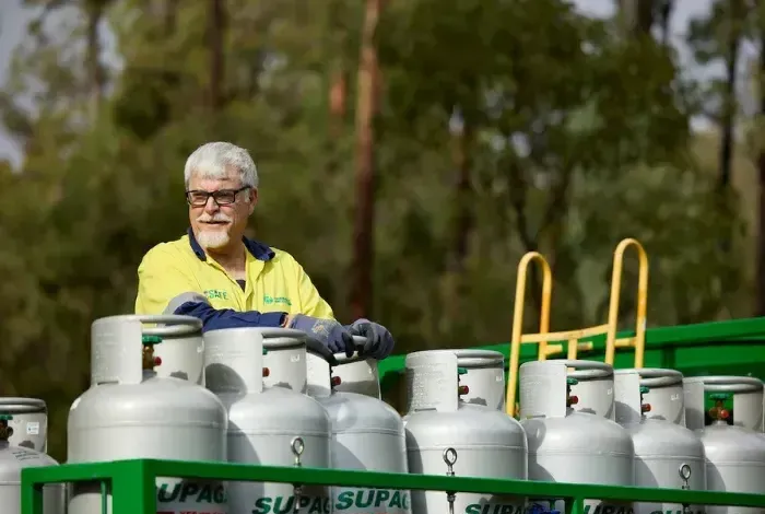 Worker in a yellow shirt standing behind rows of silver gas cylinders on a green truck. - Dunnrite Plumbing Services in Cannonvale, QLD