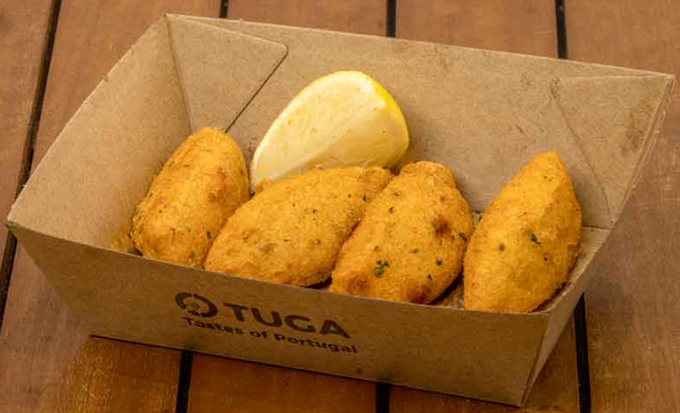 A cardboard box filled with fried food and a lemon slice on a wooden table — O Tuga Tastes Of Portugal In Melbourne, VIC