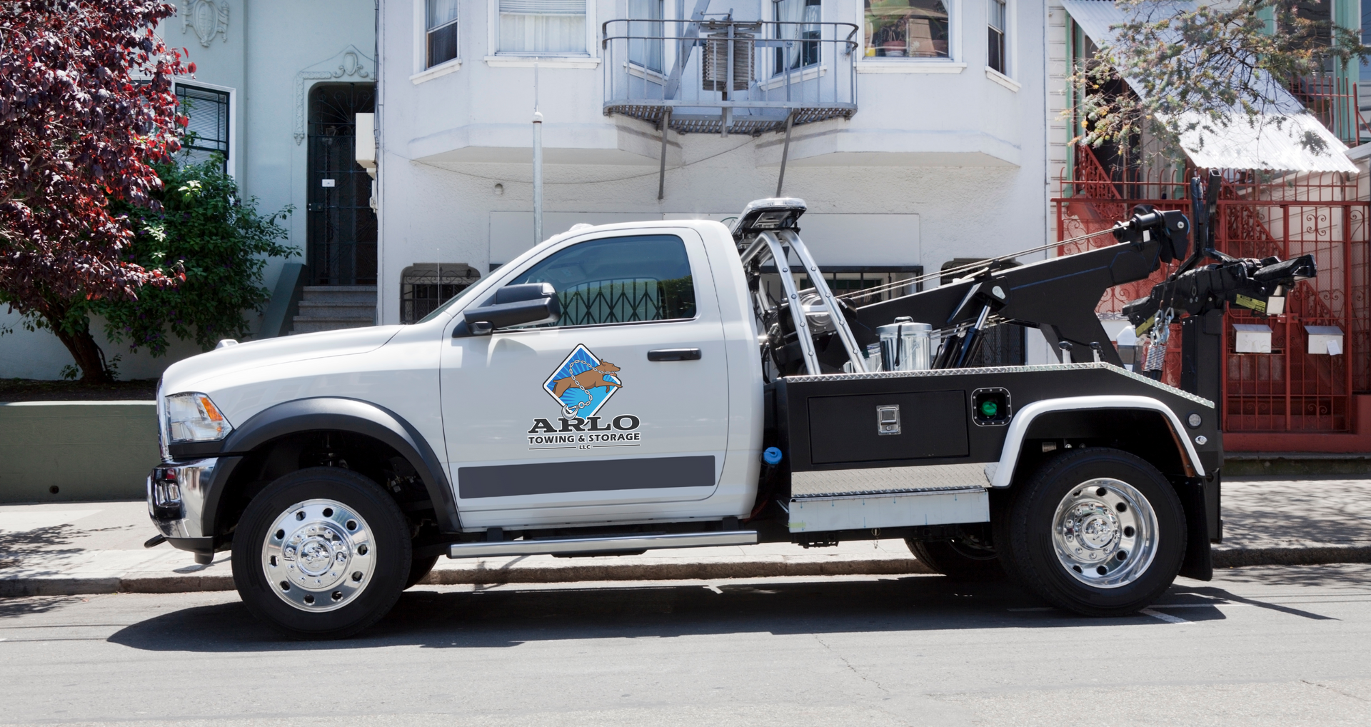 A white tow truck is parked in front of a house with the Arlo Towing and Storage logo on the side