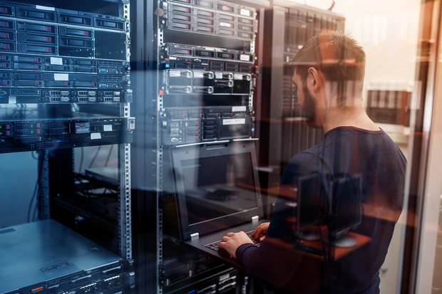 a man is working on a laptop in a server room .