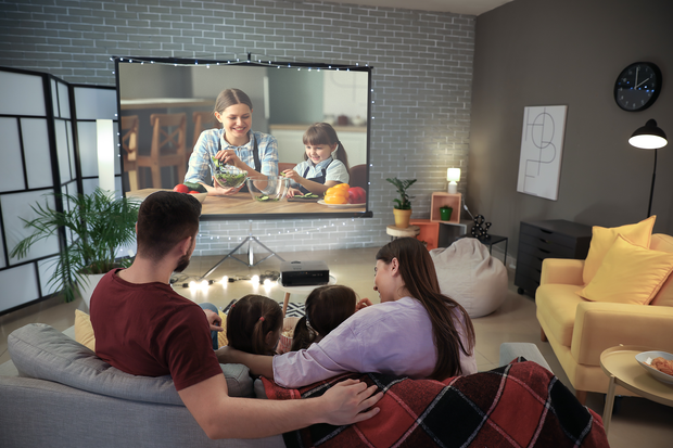 a family is sitting on a couch watching a movie on a projector screen .