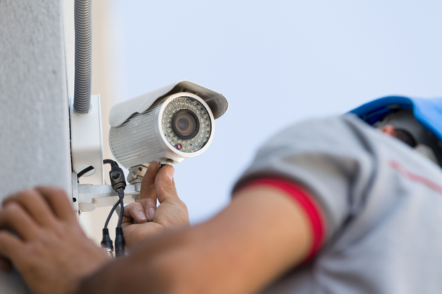 a man is installing a security camera on the side of a building .