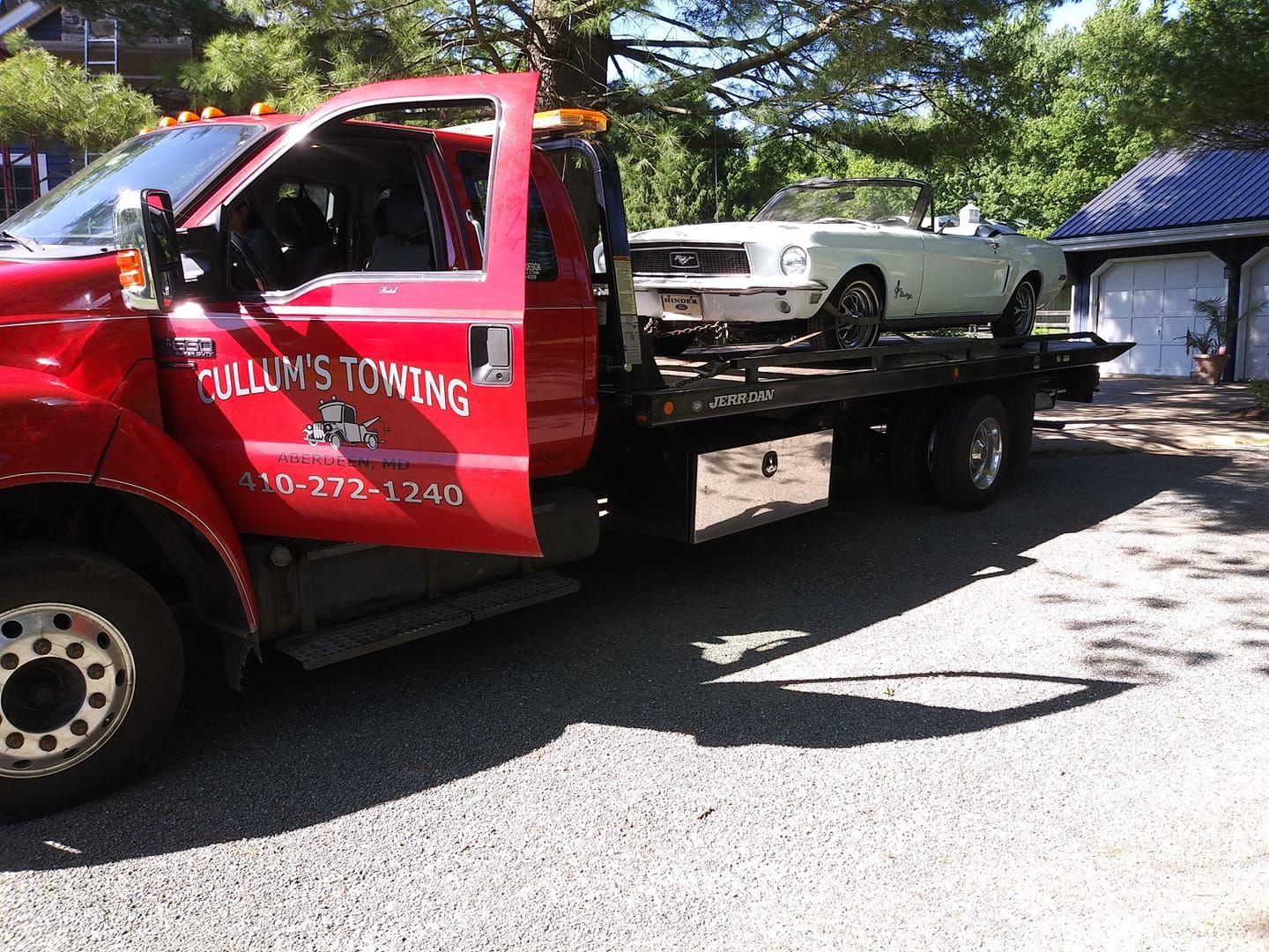 Red tow truck carrying a white car on a flatbed in a driveway, with a garage in the background