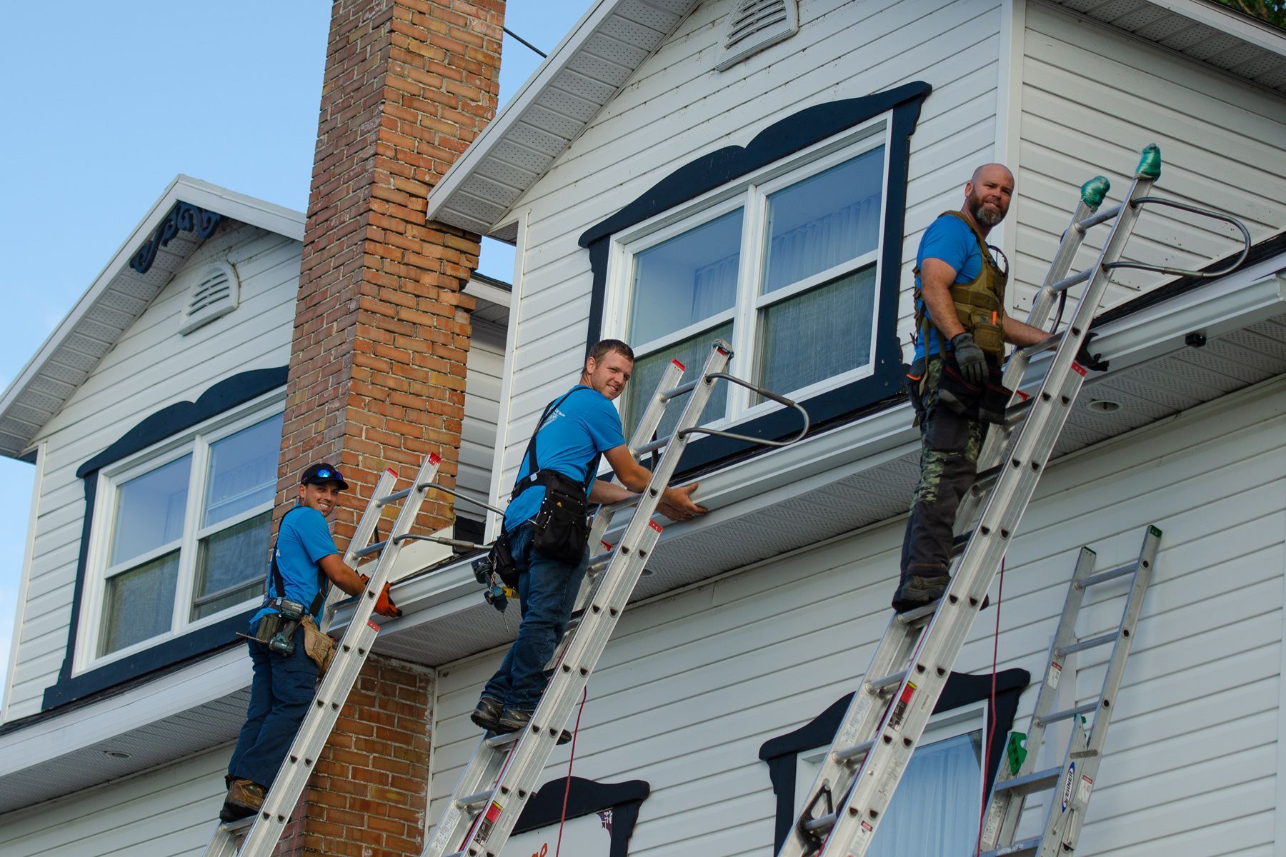 Trois hommes sont debout sur des échelles sur le côté d'une maison.