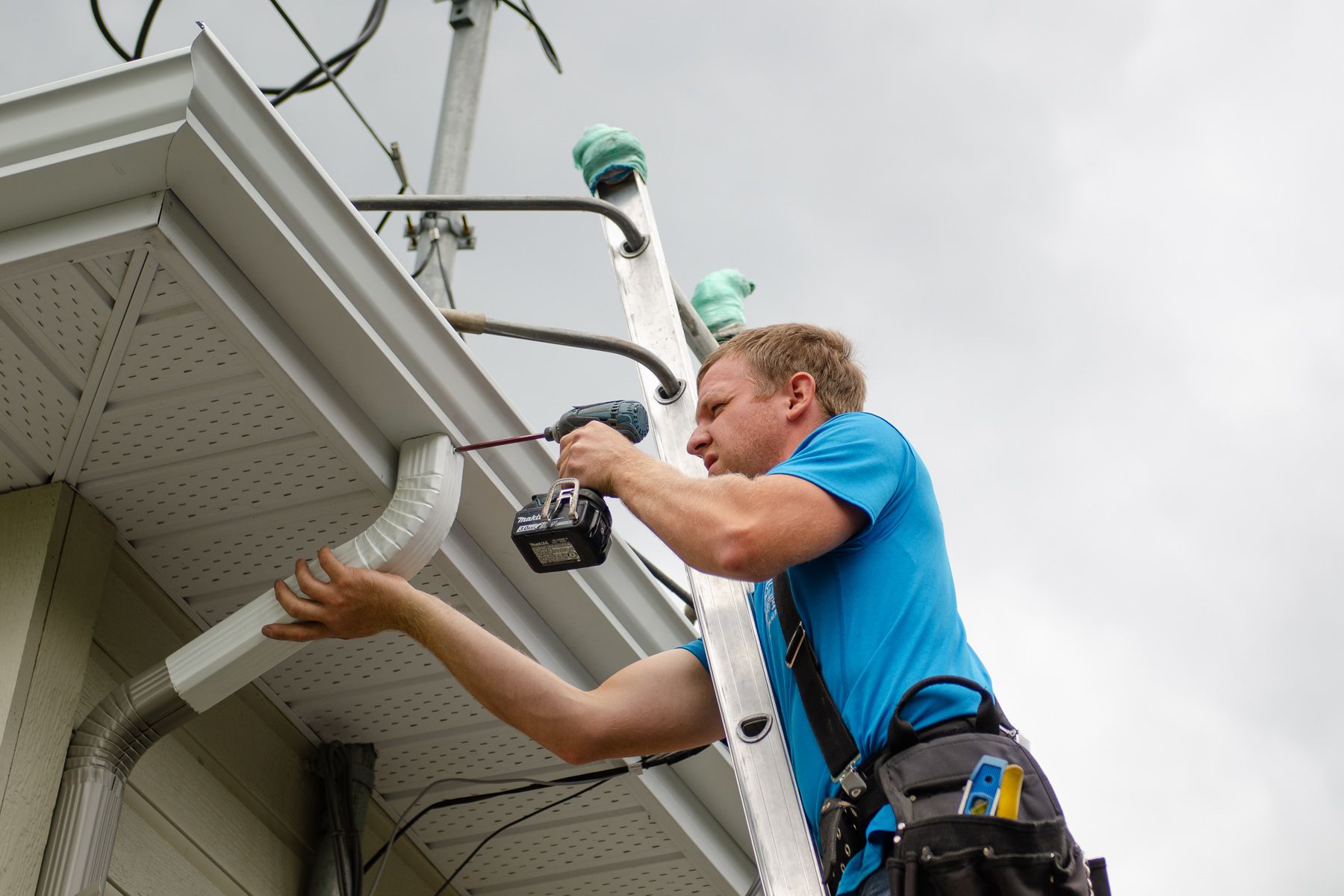 Un homme est debout sur une échelle en train de réparer une gouttière sur une maison.