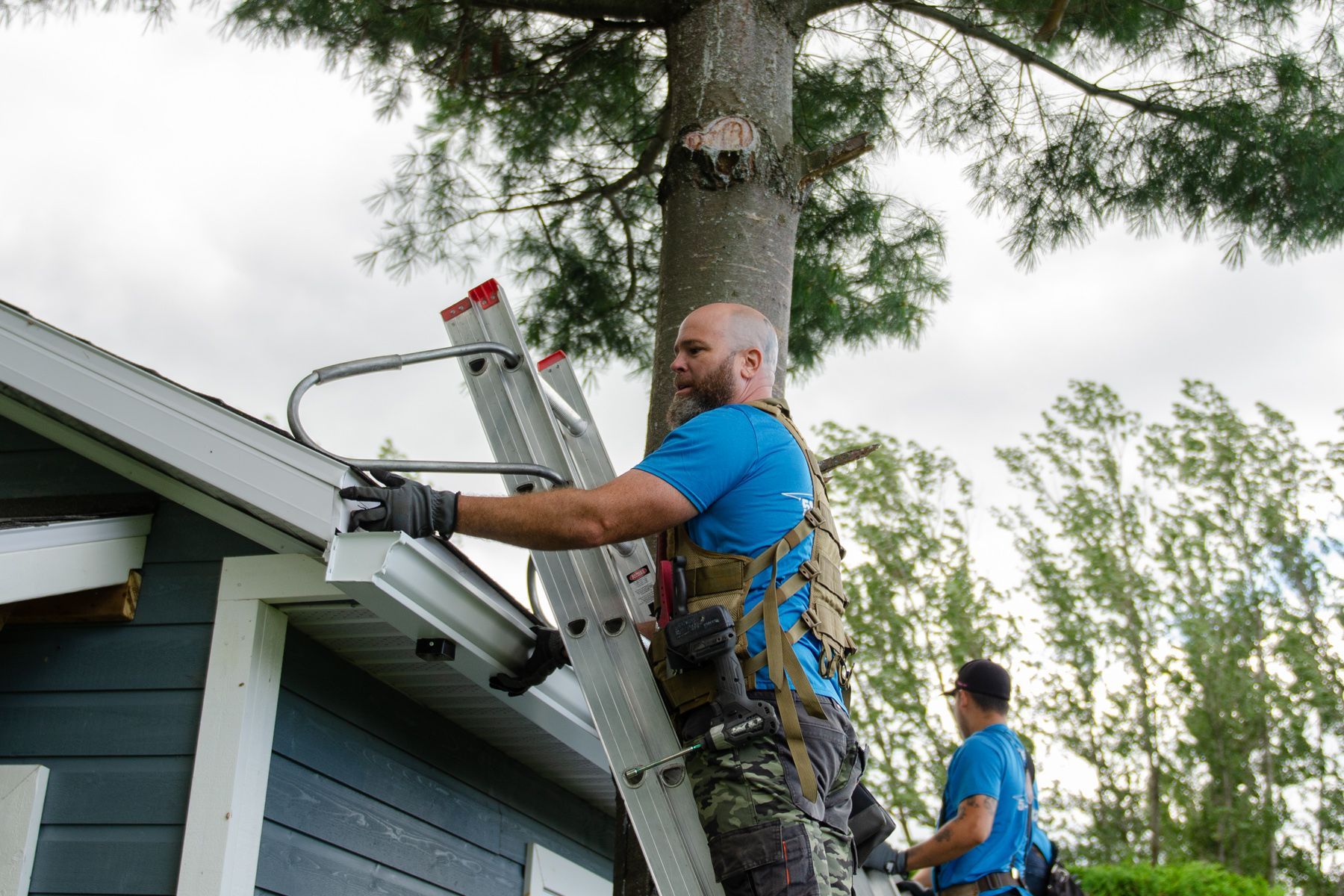 Un homme grimpe sur une échelle pour réparer une gouttière sur le toit d'une maison.