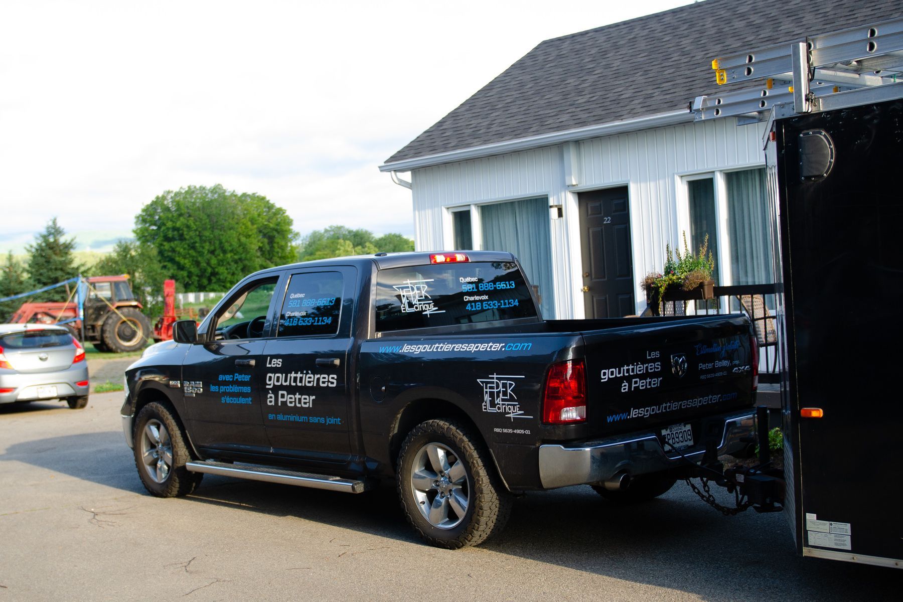 Un camion noir avec une remorque attachée est garé devant une maison.