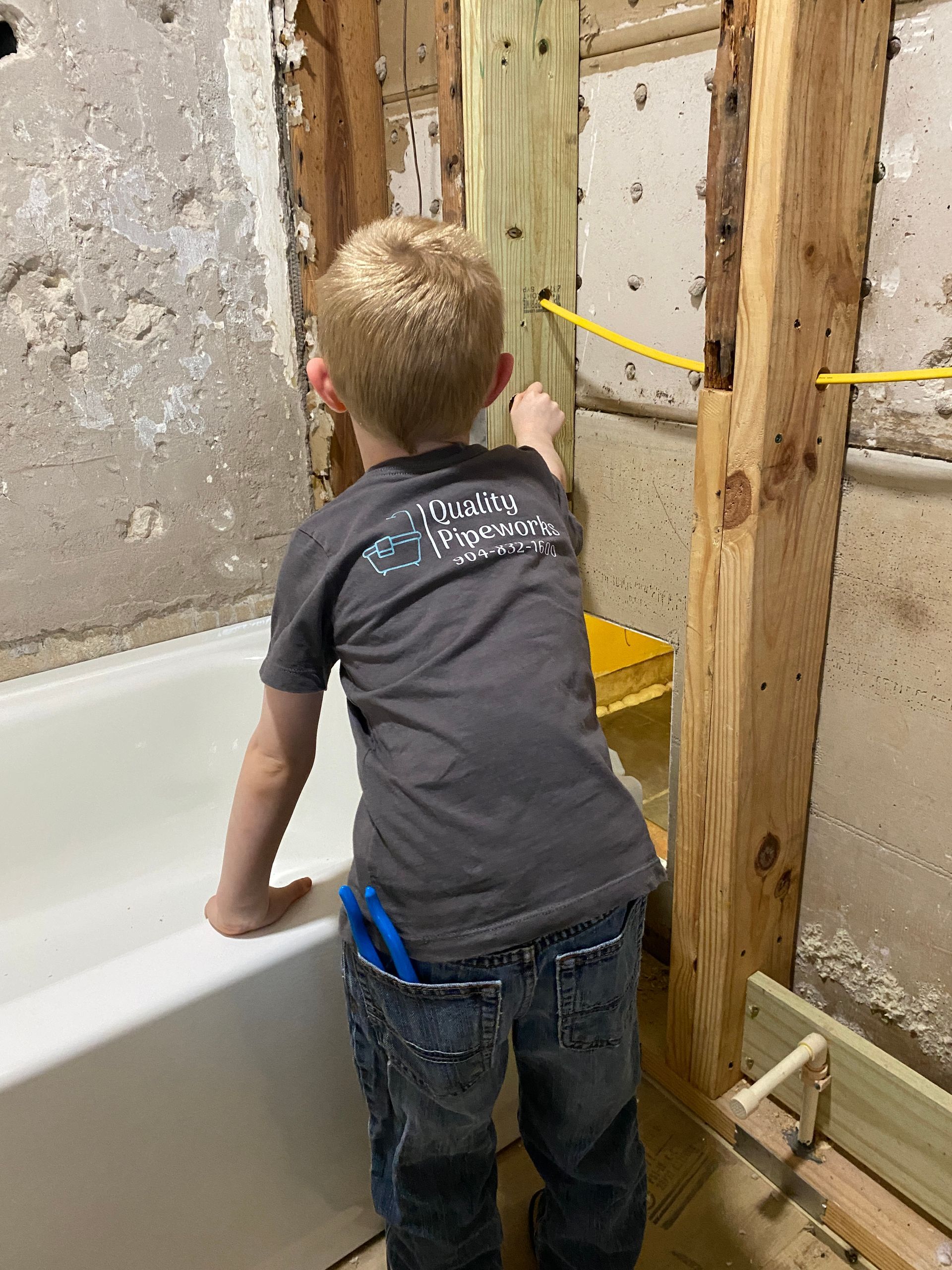 A young boy is standing next to a bathtub in a bathroom.