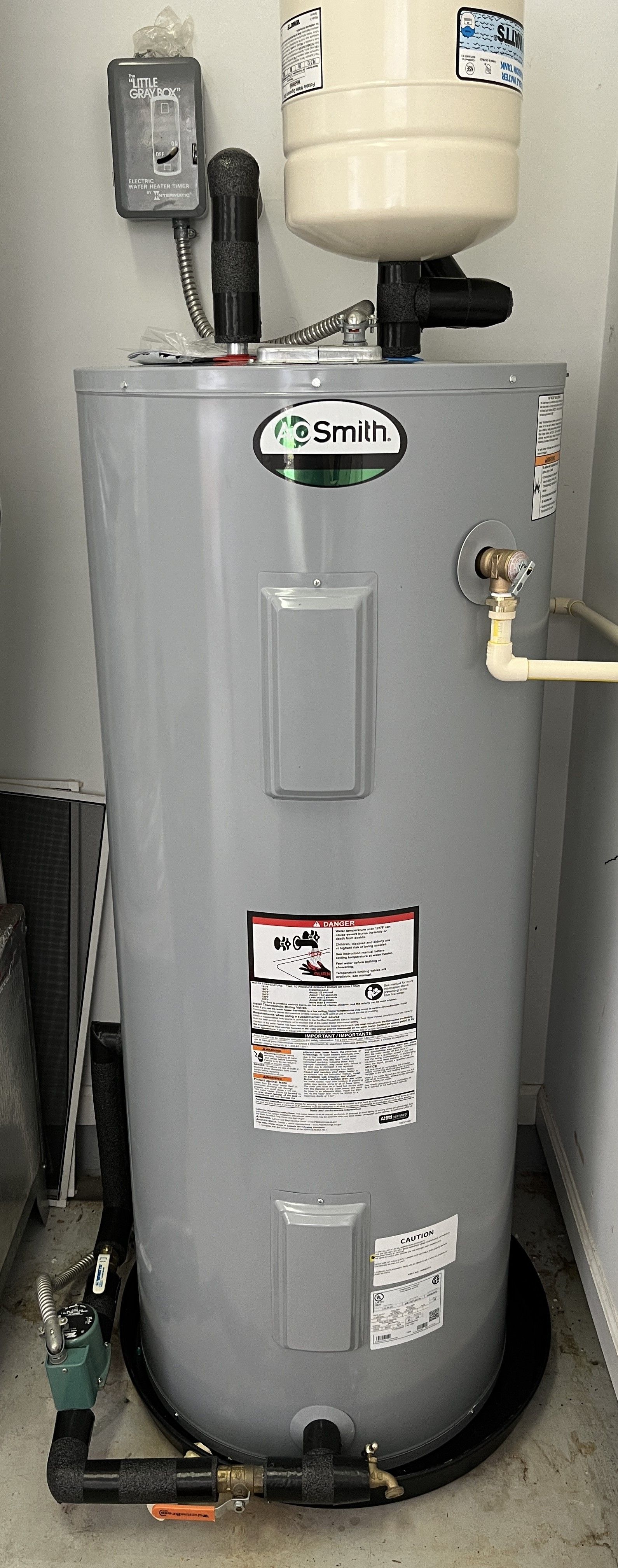 A gray water heater is sitting in a room next to a wall.