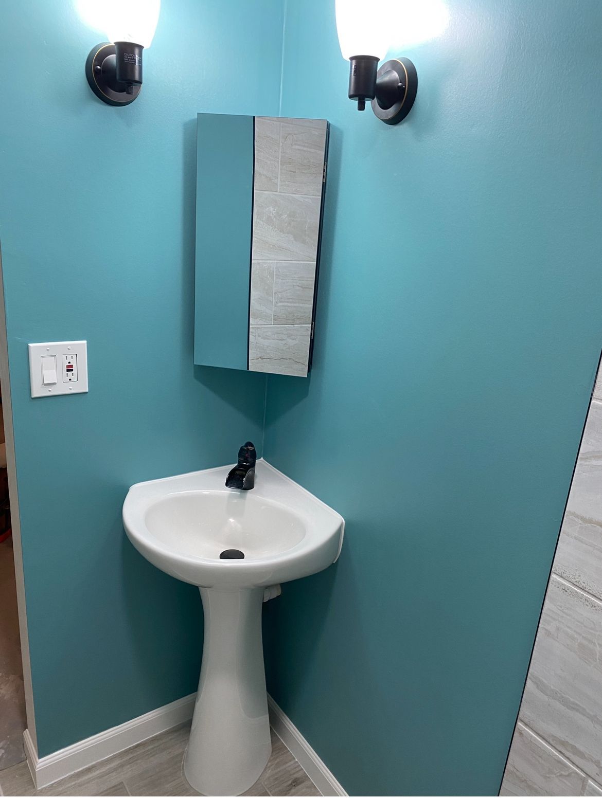 A bathroom with a pedestal sink , mirror and light.