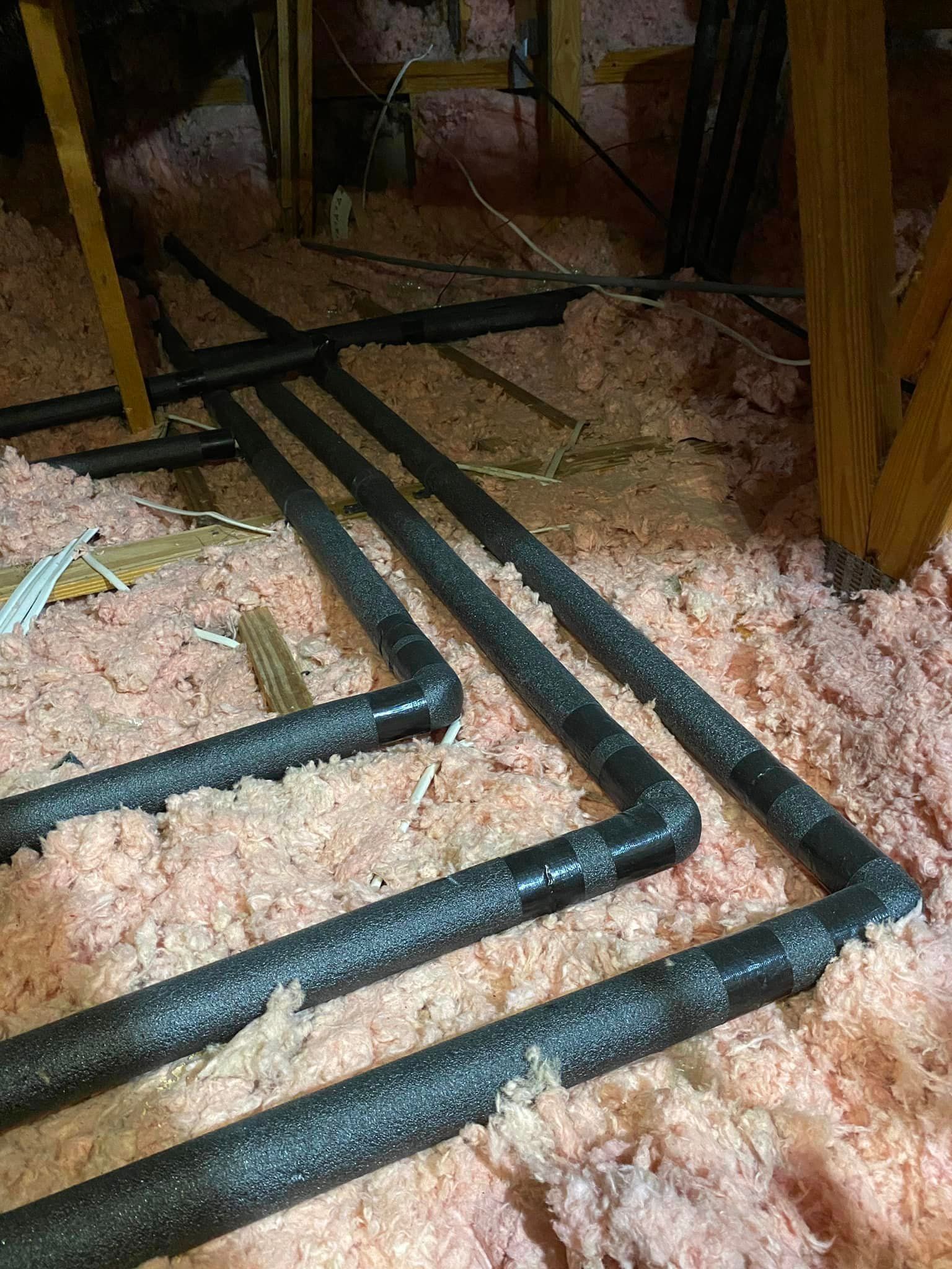 A bunch of pipes are laying on the floor in an attic.