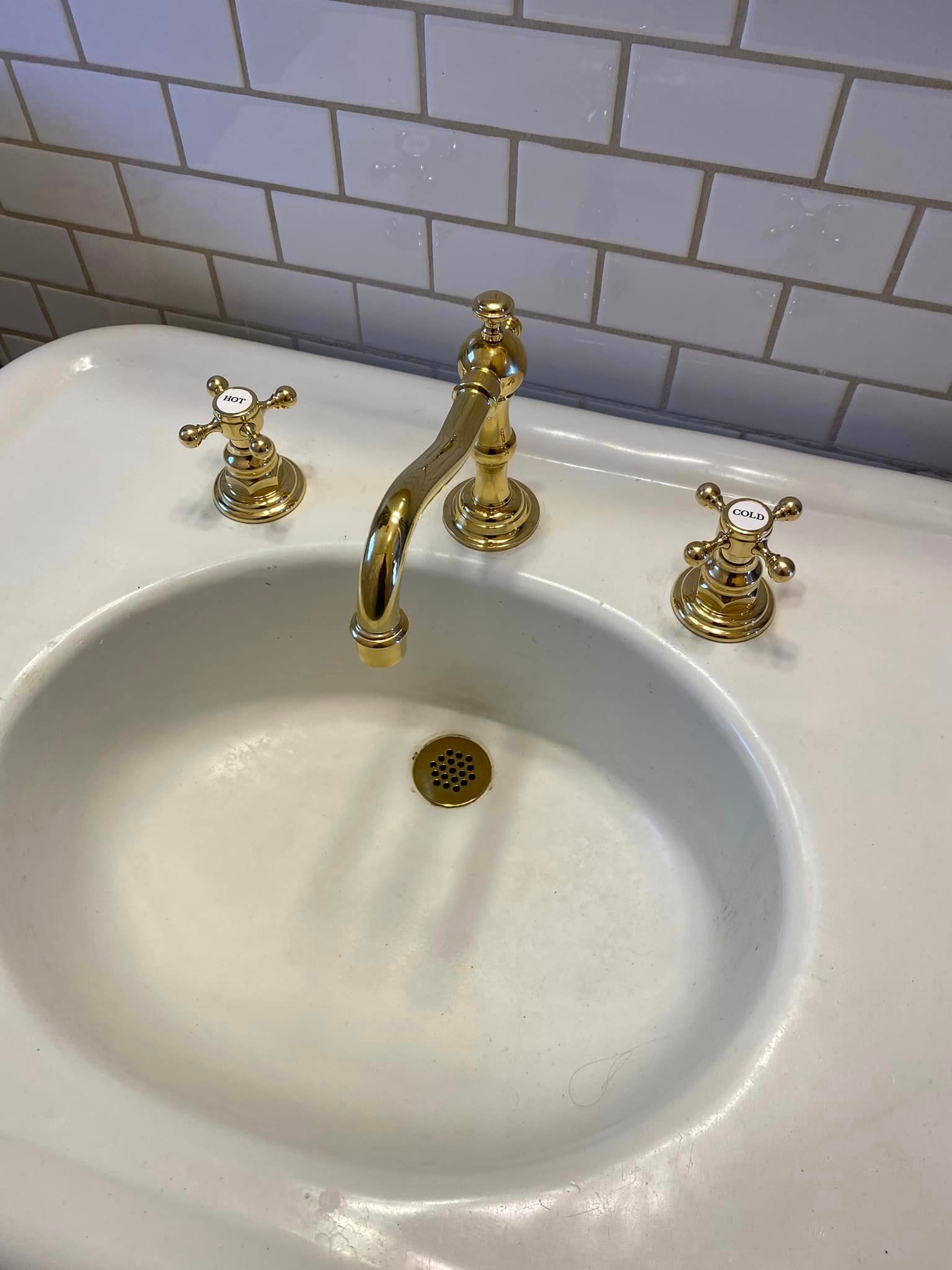 A white sink with gold faucets and handles in a bathroom.