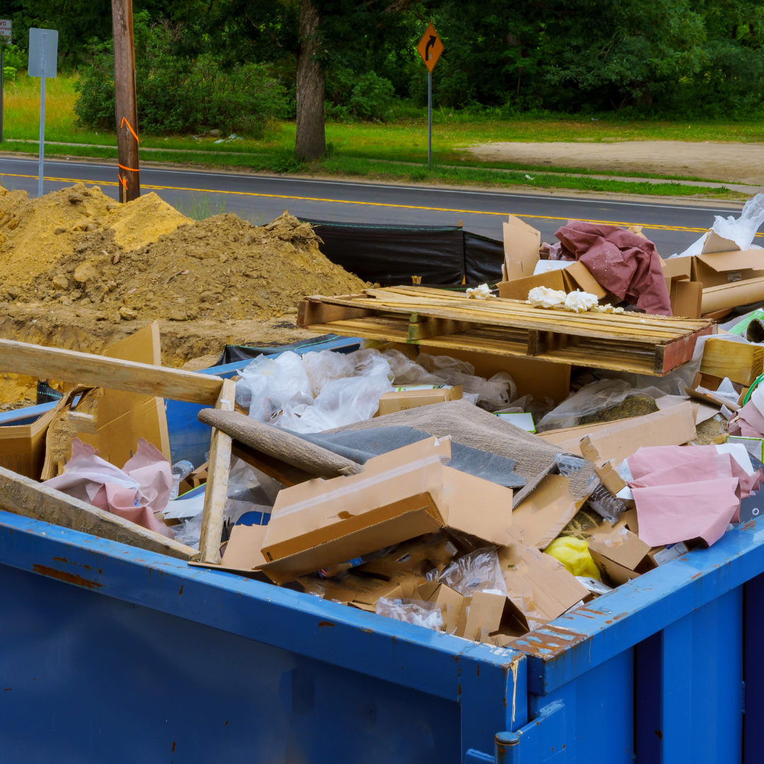 A blue dumpster filled with lots of cardboard boxes and trash.