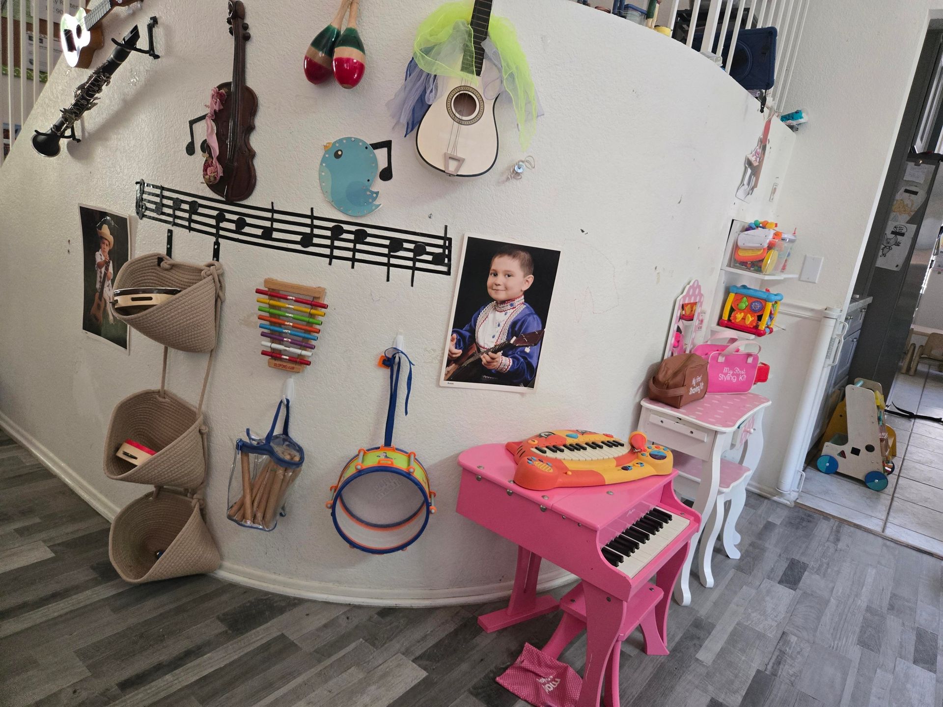 Playroom wall with hanging toys, baskets, and a pink children’s keyboard under a baby photo