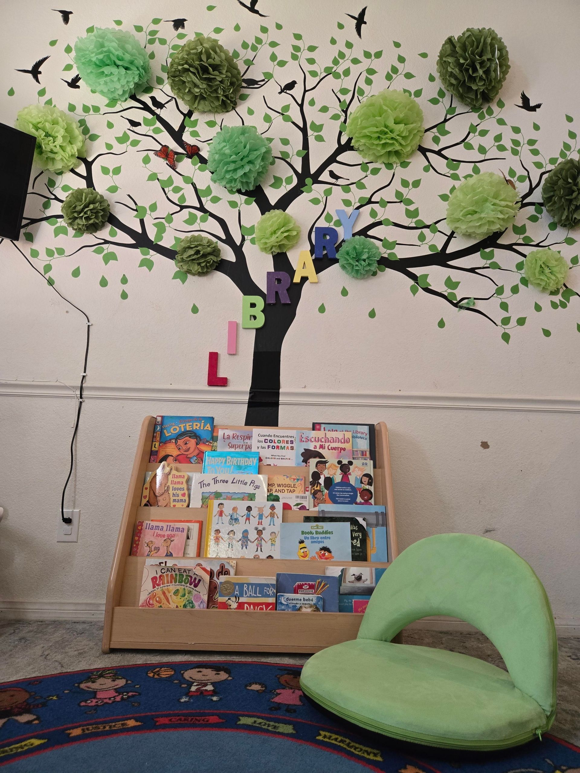 Children’s reading nook with a tree mural, bookshelf, and green chair against a wall