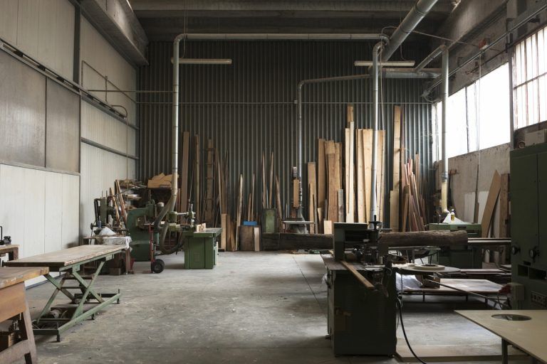 Laboratorio di falegnameria con cataste di legname, utensili e caratteristiche industriali.