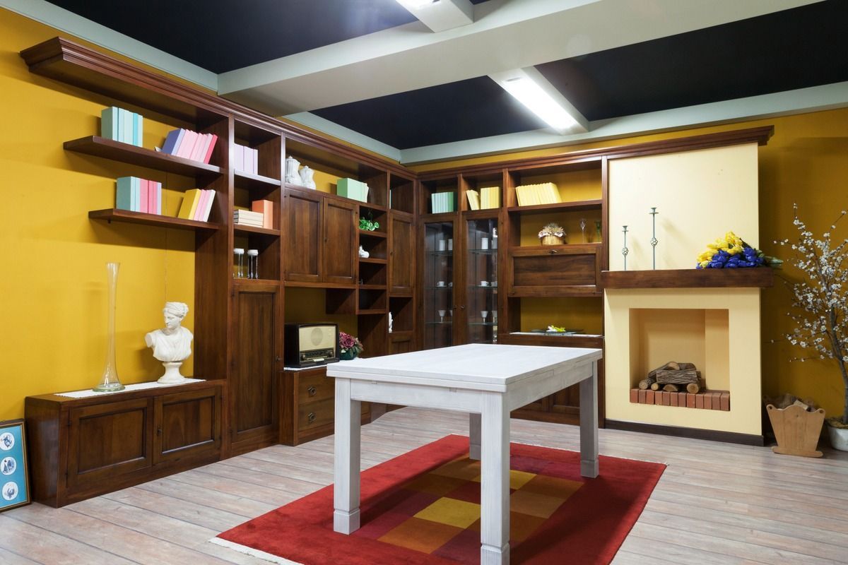 Librerie in legno e camino in una stanza con un tavolo bianco su un tappeto rosso; pareti gialle.