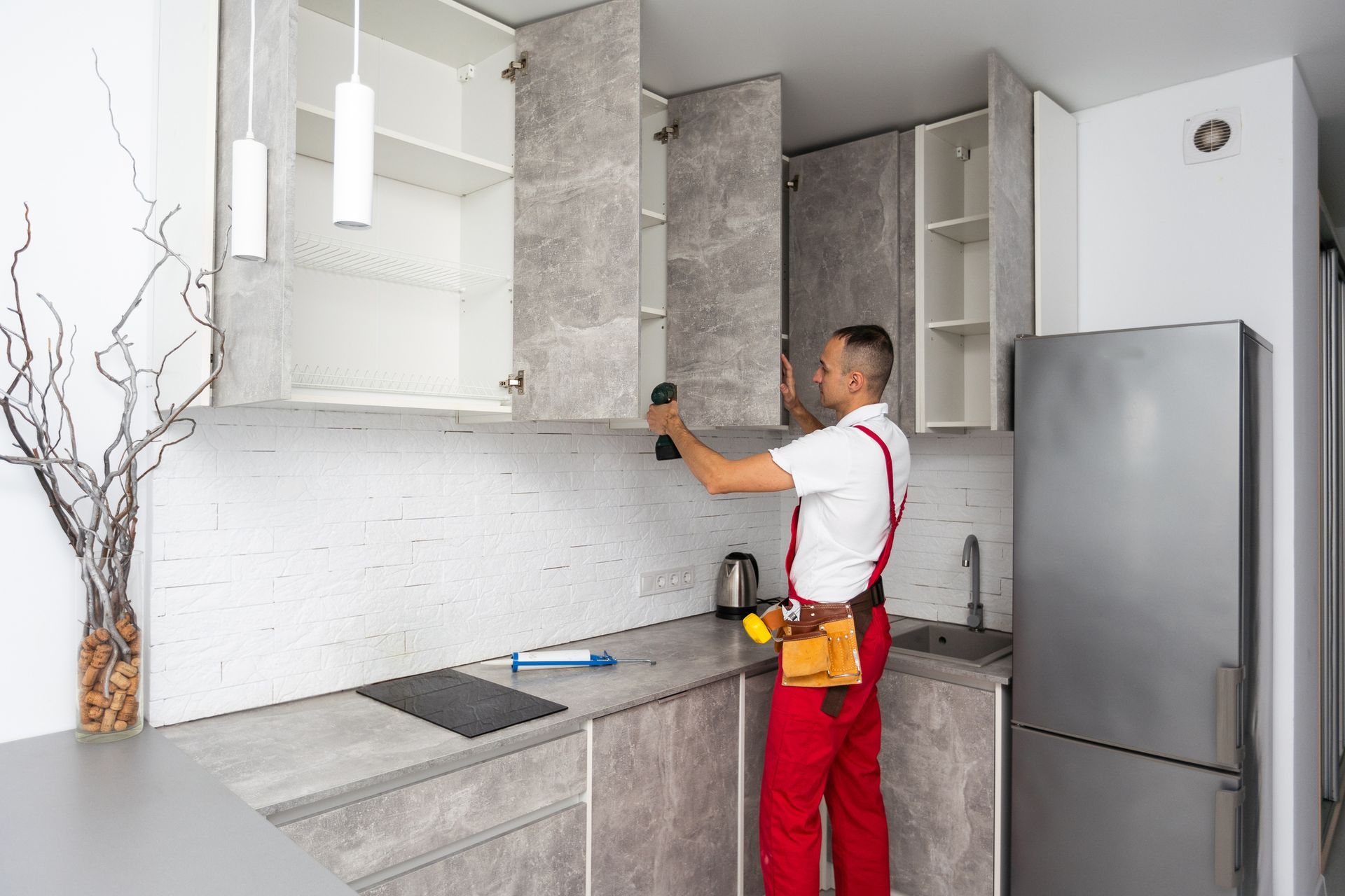 Uomo che installa l'anta di un mobile in una cucina moderna con mobili grigi e un frigorifero in acciaio inossidabile.