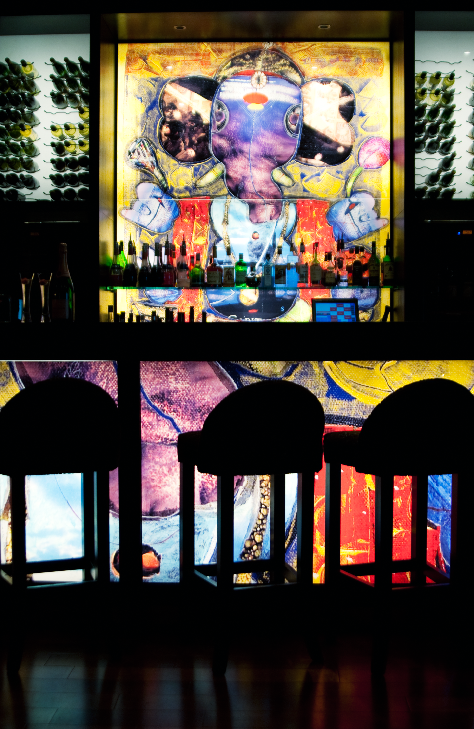 A bar with stools and a painting on the wall behind it.