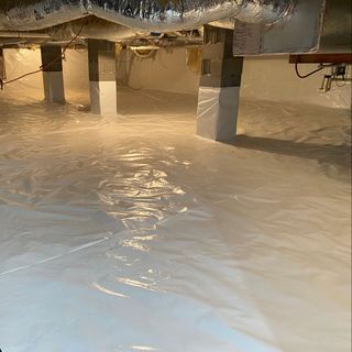 Interior view of a crawlspace with white vapor barrier material installed around support columns and across the floor.