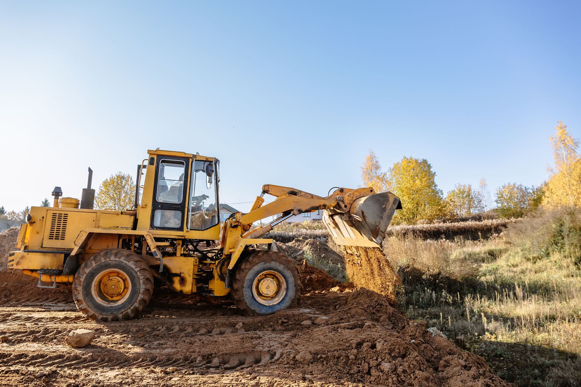 Yellow front loader scoops dirt at a construction site under a clear blue sky.
